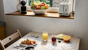 A breakfast table with croissants, fruit, coffee, and juice, a toaster, and a bowl of fruit on a window sill.