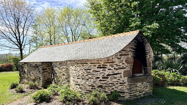 A stone building with a sloped roof, a small door, and a brick chimney.