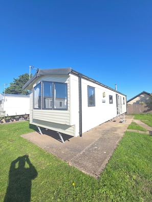 A mobile home with a covered porch, a small attached garage, and a paved driveway. - Caravan Stacey 3 BEd (Rhyl)