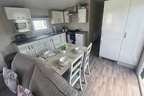 A compact kitchen with a microwave, stove, and white cabinets. - Scarlet 3 Bed Caravan Sleeps 6 - Balcony (Rhyl)