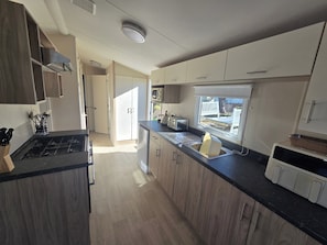 A modern kitchen with a central island, built-in appliances, and a view to the outdoors. - Caravan Stacey 3 BEd (Rhyl)