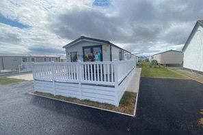 A mobile home with a fenced porch, a small deck, and a grassy yard. - Scarlet 3 Bed Caravan Sleeps 6 - Balcony (Rhyl)