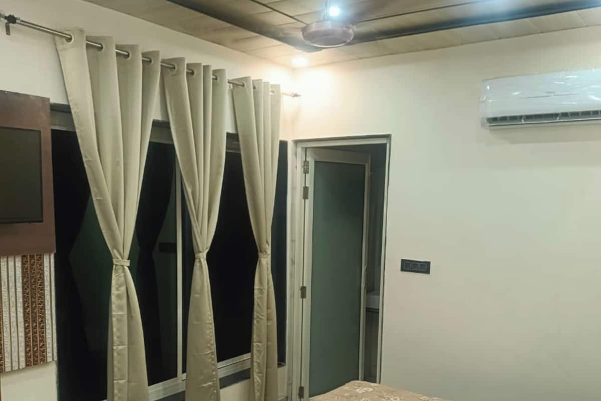 A bedroom with a bed, curtains, a ceiling fan, and an air conditioning unit.