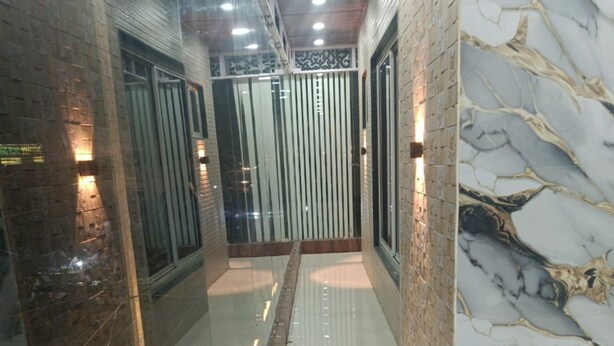 Un pasillo con suelo de baldosas reflectantes, pared de mármol y mampara de vidrio con persianas verticales.