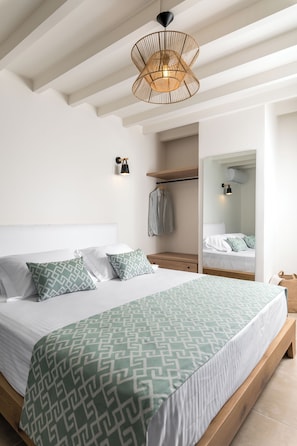 A modern bedroom with a large bed, a hanging light fixture, a wardrobe, and a mirror. - Amvikas: Ampelos Suite-Sitia (Sarantapichos)