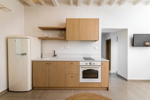 A modern kitchen with a built-in oven, a white refrigerator, wooden cabinets, and a countertop. - Amvikas: Ampelos Suite-Sitia (Sarantapichos)