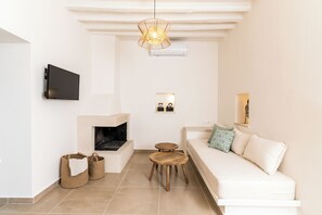 A modern living room with a fireplace, a sofa, a TV mounted on the wall, and a hanging light fixture. - Amvikas: Ampelos Suite-Sitia (Sarantapichos)