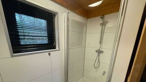 A glass-enclosed shower with a handheld showerhead, a window with blinds, and white tiled walls. - Holiday Home in Velsen-zuid With Terrace (Velsen-Zuid)