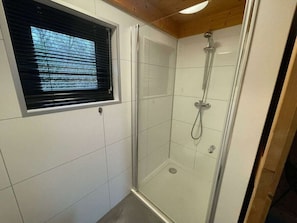 A glass-enclosed shower with a handheld showerhead, a window with blinds, and white tiled walls. - Holiday Home in Velsen-zuid With Terrace (Velsen-Zuid)