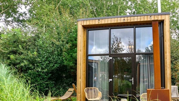 A modern, wooden-framed structure with large glass windows, outdoor seating, and a garden setting. - Holiday Home in Velsen-zuid With Terrace (Velsen-Zuid)