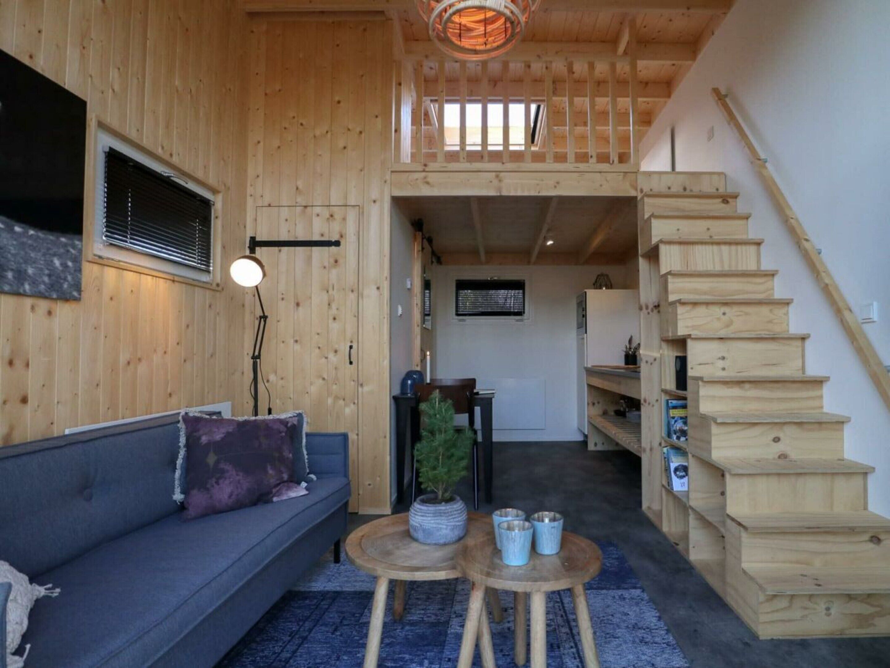 A wooden interior with a sofa, a small table, a staircase, and a view of the outside.