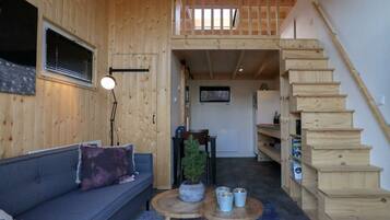A wooden interior with a sofa, a small table, a staircase, and a view of the outside.