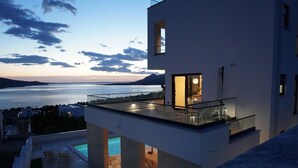 A modern building with a glass balcony overlooking a pool and a body of water. - Villa Bella Vista with heated pool (Rovanjska)