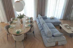A modern living room with a dining table set for four, a grey sofa, and a wooden floor.