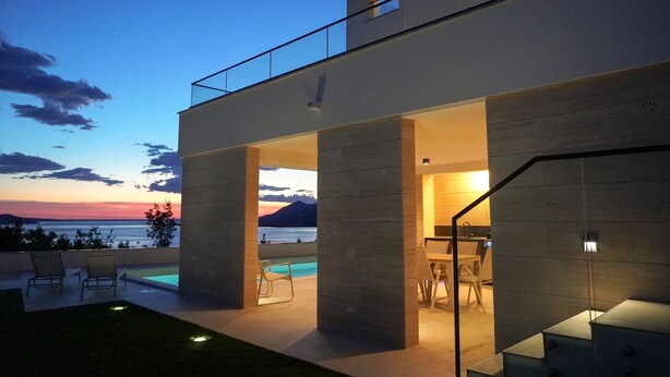 A modern building with a pool, outdoor seating, and a view of the sea. - Villa Bella Vista with heated pool (Rovanjska)