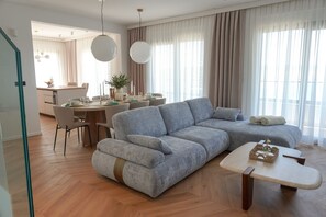 Un salon moderne avec un canapé d’angle gris, une table basse en bois et un coin repas avec une table dressée pour quatre personnes.