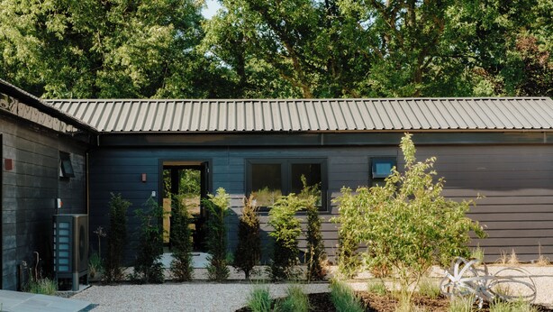 Ein modernes Gebäude mit einem Metall-Dach, einer Holztür und einem Kiesgarten mit verschiedenen Pflanzen.