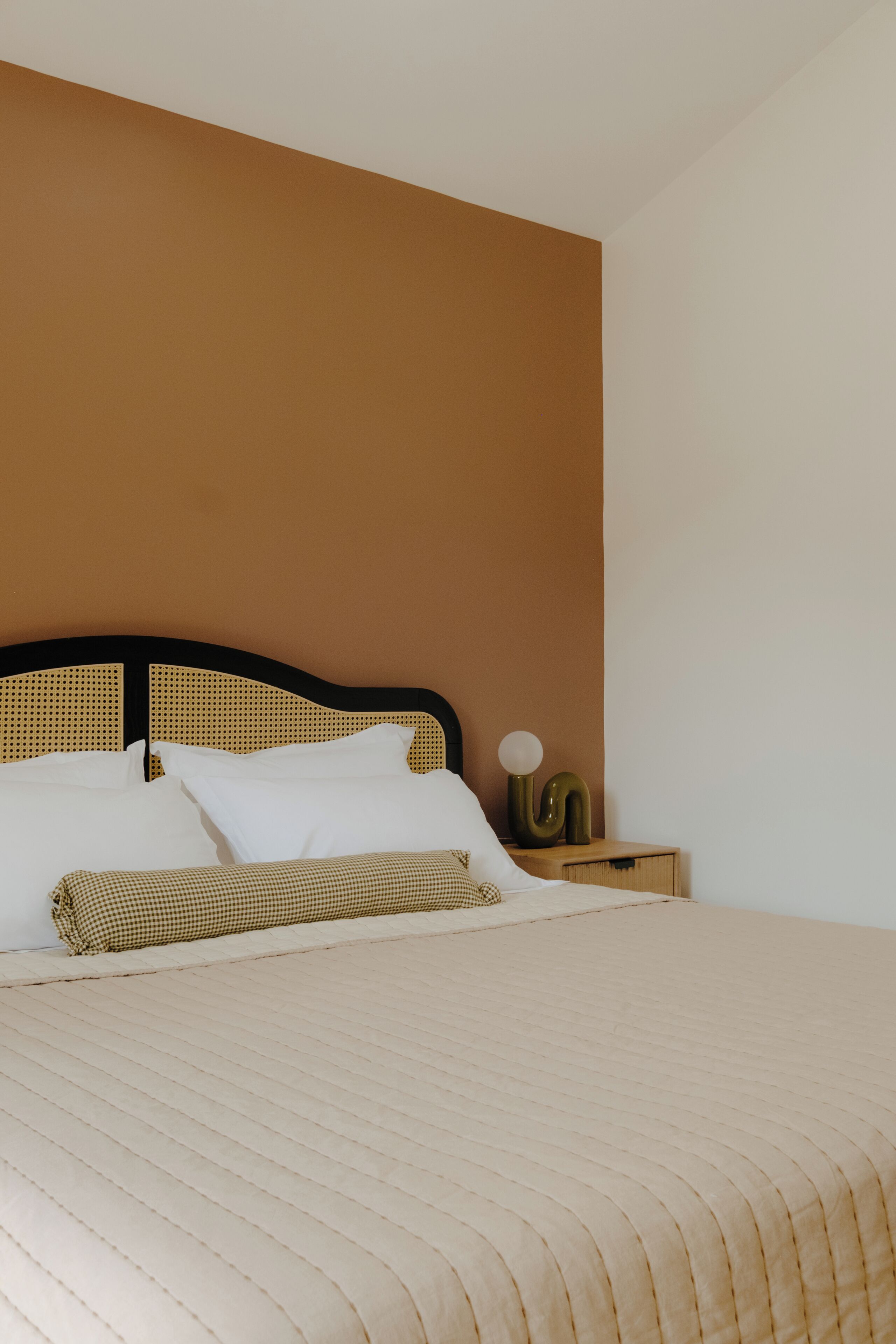 Un letto rifatto con un cuscino a quadretti, una lampada da comodino e un piccolo oggetto decorativo.