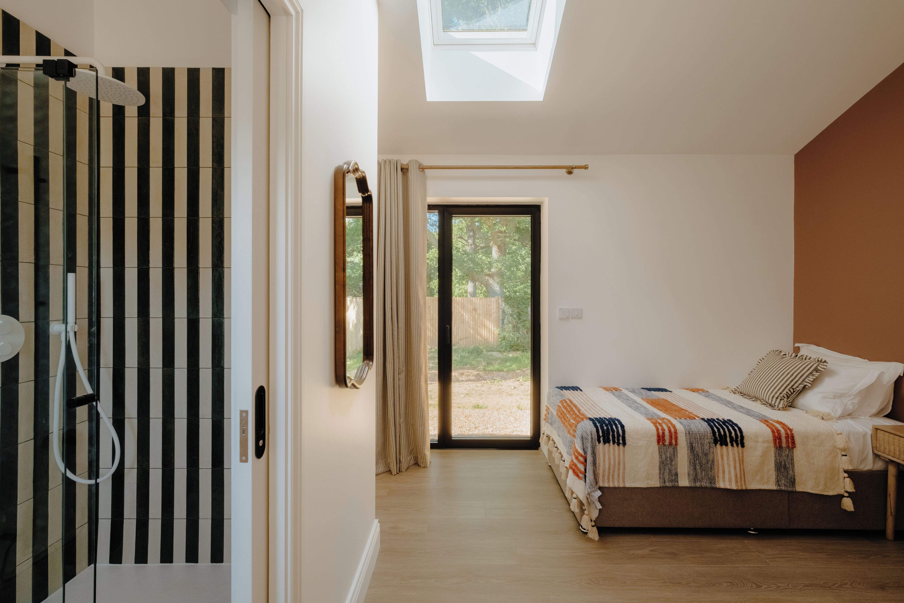 A bedroom with a skylight, a shower, a bed with a striped blanket, and a view of the outdoors.
