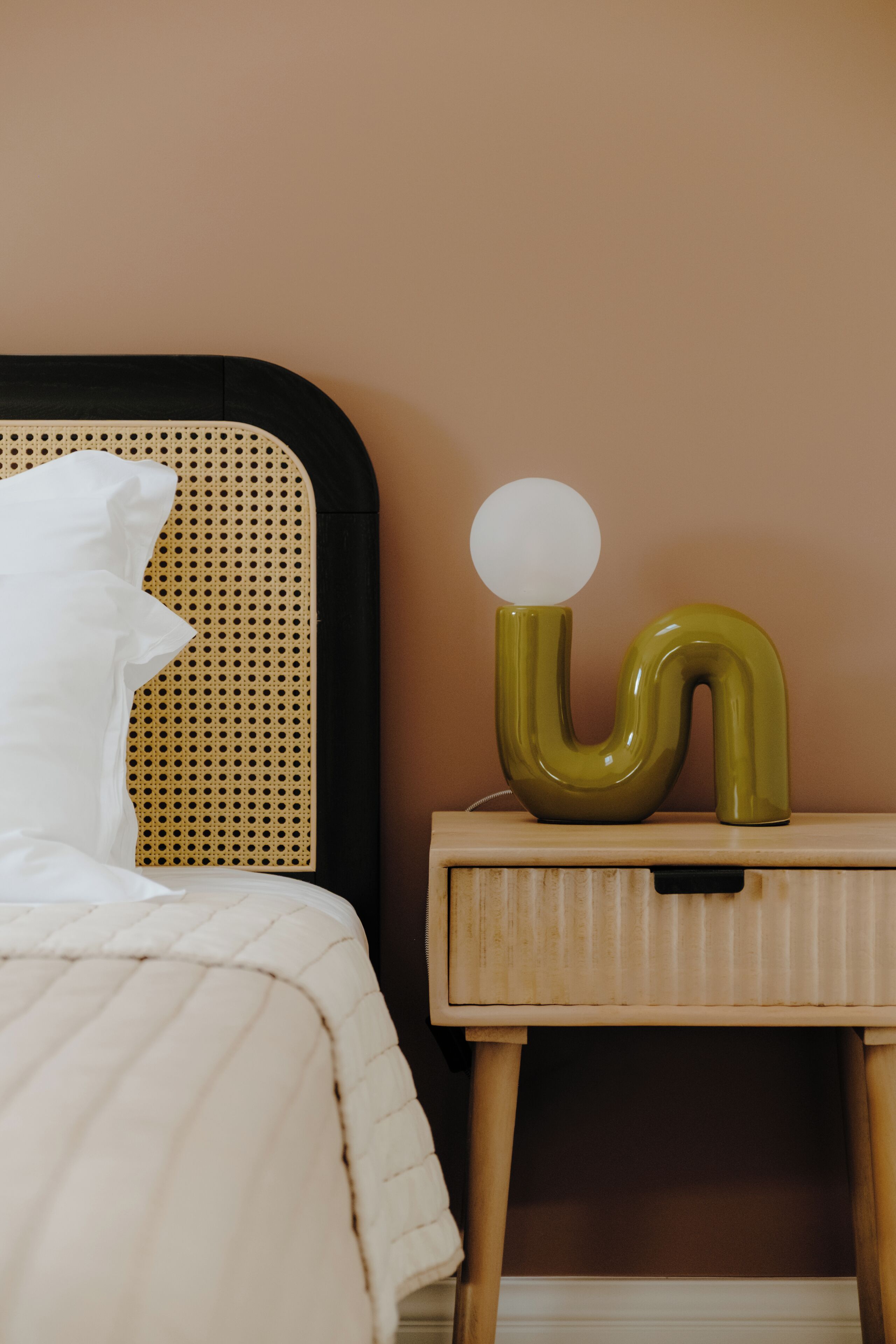 A bed with a white pillow and a bedside table with a green lamp.