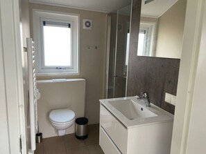 Ein kleines Badezimmer mit Toilette, einem kleinen Mülleimer, einem Fenster und einer Badewanne.