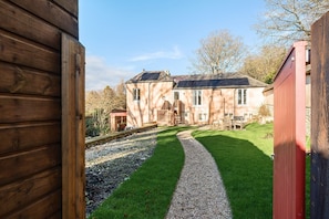 A wooden building with a gravel path leading to a house with a red door. - Artist's Studio (2) - Piddlehinton, Dorchester, sleeps 2 guests  in 1 bedroom (Piddlehinton)