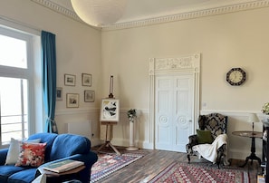 A room with a blue sofa, a patterned rug, a white door, and a clock on the wall. - Artist's Studio (2) - Piddlehinton, Dorchester, sleeps 2 guests  in 1 bedroom (Piddlehinton)