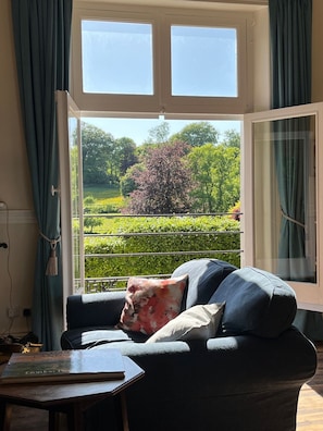 A room with a sofa facing a large window with a view of a garden. - Artist's Studio (2) - Piddlehinton, Dorchester, sleeps 2 guests  in 1 bedroom (Piddlehinton)