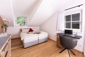 A bedroom with a bed, a desk, a chair, a window, and a view of greenery outside. - Vrbo Property (Schönau am Königssee)