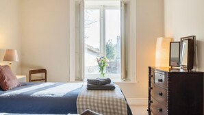 Ein Schlafzimmer mit Bett, Kommode, Lampe und Fenster mit Blick.