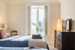Ein Schlafzimmer mit Bett, Kommode, Lampe und Fenster mit Blick.