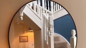 Un miroir rond reflète un escalier avec des balustrades blanches et un mur sombre.