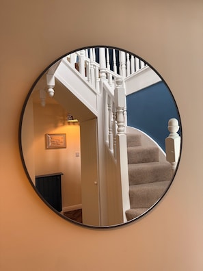 A circular mirror reflecting a staircase with white balusters and a dark wall.