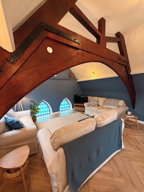 Ein gemütliches Schlafzimmer im Loft-Stil mit freiliegenden Holzbalken, einem großen Bett, einer Couch und einem Fernseher.