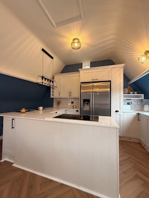 Une cuisine moderne avec des meubles blancs, un îlot central, des appareils en acier inoxydable et des luminaires suspendus.