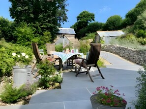 An outdoor patio with a table and chairs, surrounded by greenery and a stone wall. - Foxearth (2) - sleeps 2 guests in 1 bedroom, Winterborne Houghton, Dorset (Blandford Forum)