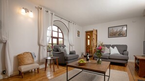 Una sala de estar con dos sofás grises, una mesa de centro de madera, una silla de mimbre y una pequeña mesita auxiliar.