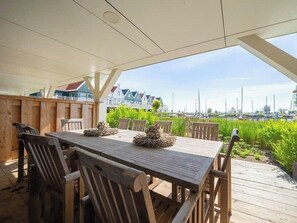 Eine Holzterrasse mit Tisch und Stühlen, mit Blick auf einen Yachthafen mit Booten und Häusern.