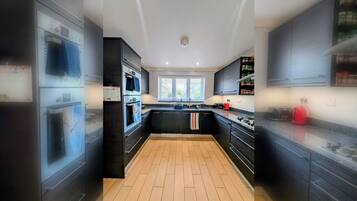 Cocina moderna con armarios negros, suelo de madera con diseño de espiga, una isla central y una ventana con persianas.