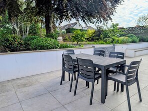 An outdoor patio area with a table and chairs, surrounded by greenery and a white wall. - Stylish 5BDR Retreat with Parking and Fast WiFi (Greater London)
