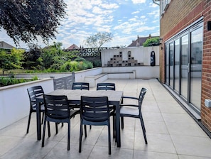 Eine Terrasse mit Tisch und Stühlen, eine Ziegelwand und eine Glastür.