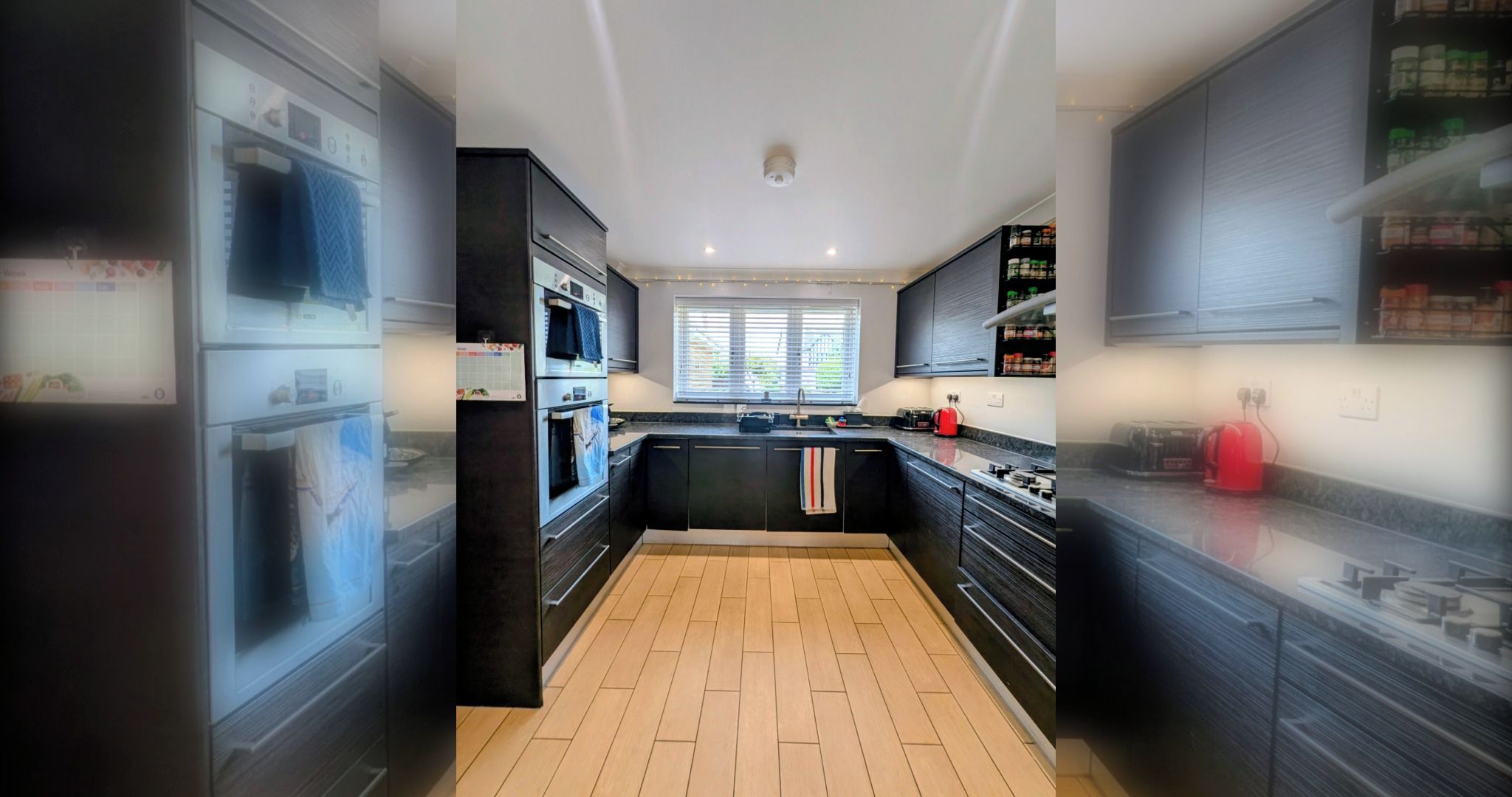 A modern kitchen with black cabinetry, a wooden herringbone floor, a central island, and a window with blinds.