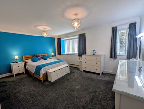 A bedroom with a bed, bedside tables, a dresser, a mirror, and a window with curtains. - Stylish 5BDR Retreat with Parking and Fast WiFi (Greater London)