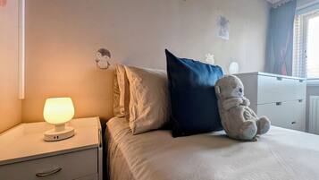 Un dormitorio con una cama, una lámpara de noche, un osito de peluche y un aparador con cajones.