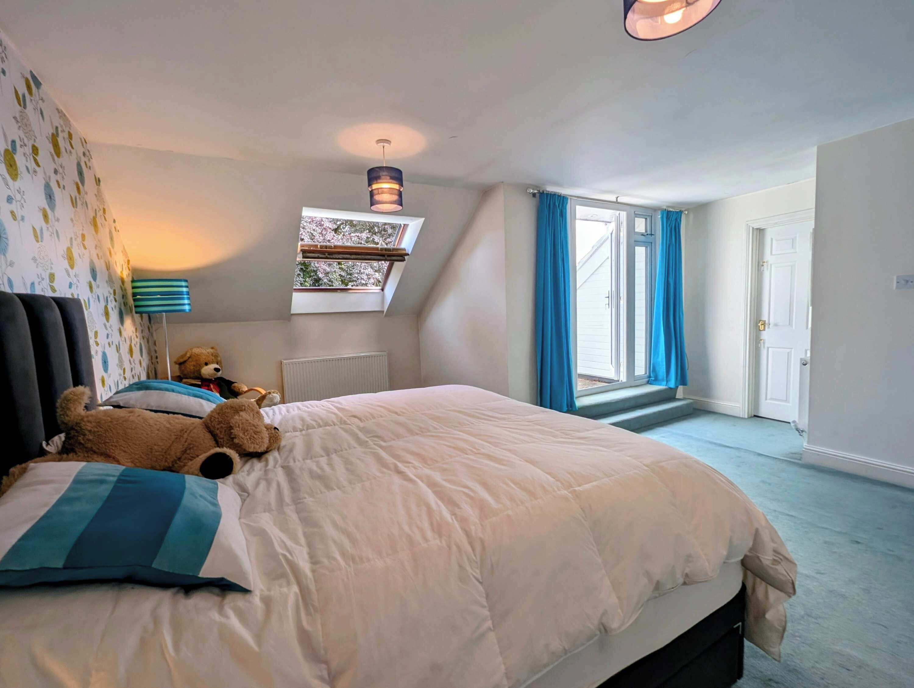 Un dormitorio con cama, ventana, un osito de peluche y un radiador.