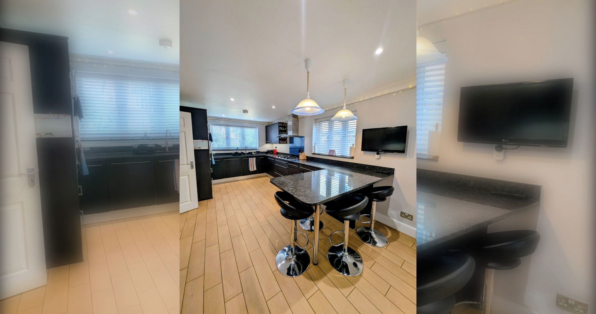 A modern kitchen with a central island, bar stools, pendant lighting, and a flat-screen TV mounted on the wall.