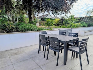 Eine Terrasse im Freien mit Tisch und Stühlen, umgeben von Grünpflanzen und einer weißen Mauer.