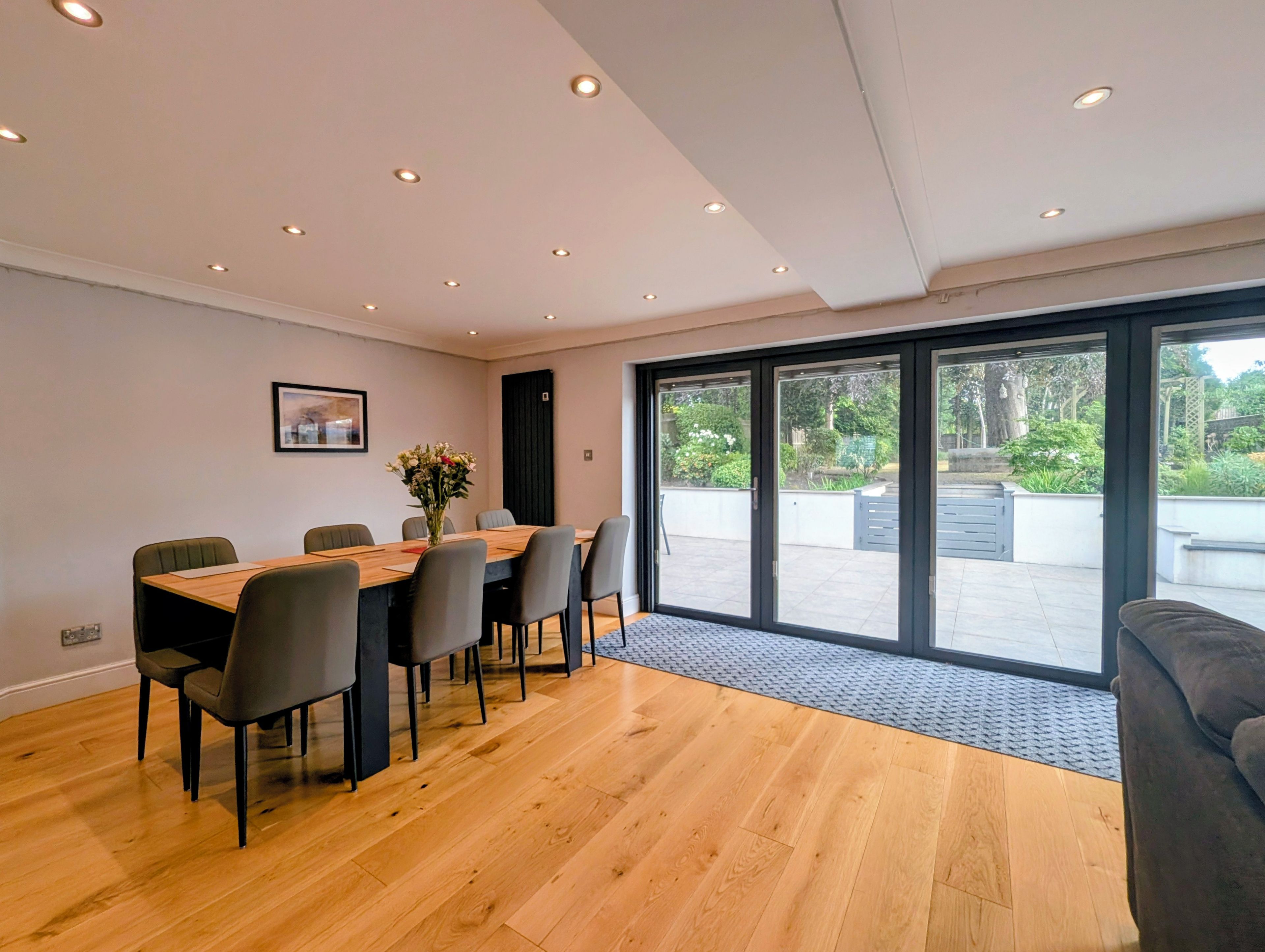 A modern dining area with a wooden table, chairs, and a view of the outdoors through large sliding glass doors.
