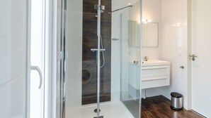 A modern bathroom with a glass-enclosed shower, a white vanity, and a dark wood accent wall. - Holiday Home in Brunssum With Terrace (Brunssum)