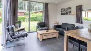 A modern living room with a sofa, a coffee table, and a dining table. There is a large window with curtains, and a painting on the wall. - Holiday Home in Brunssum With Terrace (Brunssum)